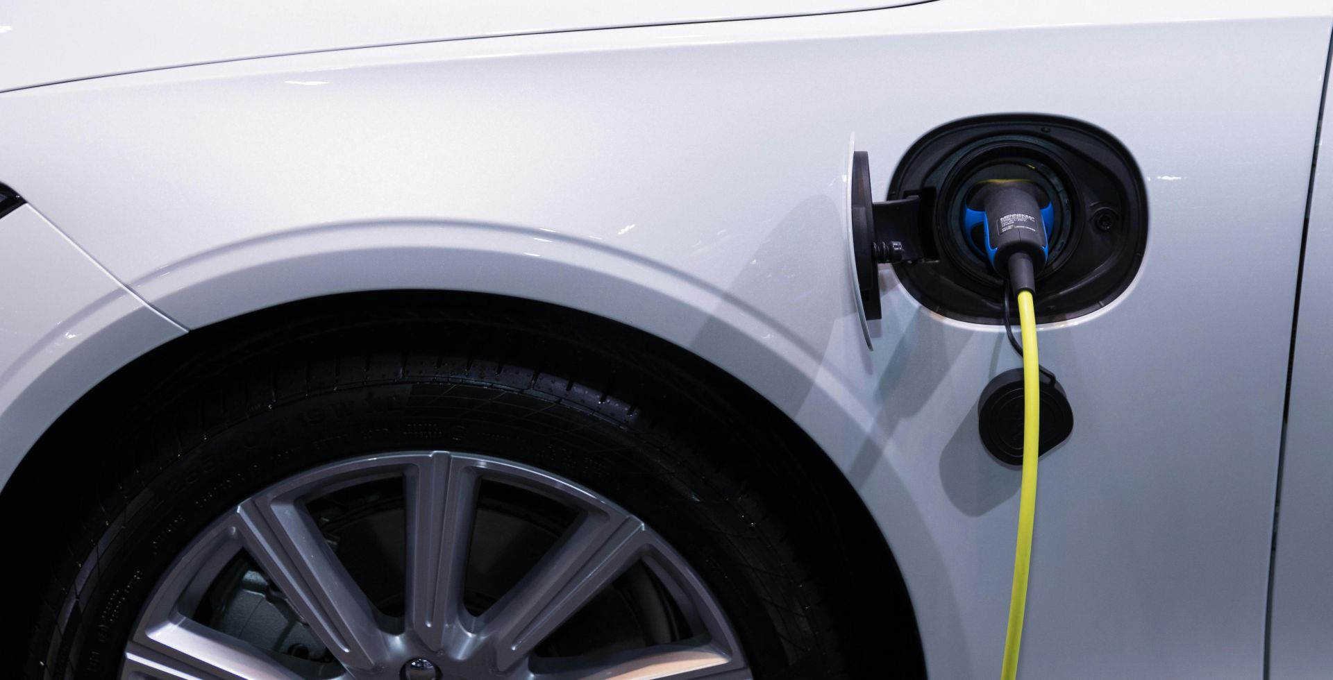 A white electric car is plugged in for charging, close-up view of the charging port.